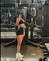 Woman in athletic wear posing in a gym with weight training equipment in the background