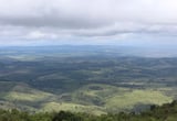 Aerial landscape view of rolling green hills and valleys with forests under a cloudy sky